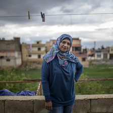 Smiling woman stands underneath clothes line outdoors with buildings and cloudy sky in background