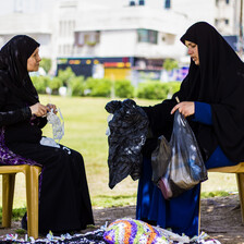 Women sit on chairs while crocheting and holding up plastic