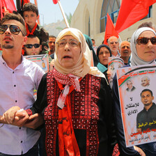 Elderly woman wearing traditional embroidered dress is flanked by two younger relatives at rally