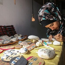 Sitting young woman writes with a pen on a rock while sitting at a table filled with illustrated rocks