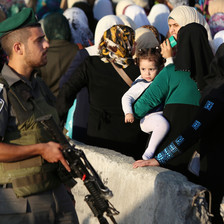 Israeli soldier carrying gun stands in front of queue of women and children at checkpoint