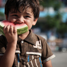 A smiling young boy eats a slice of watermelon