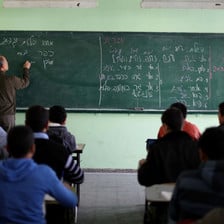 Man writes words in Hebrew on chalkboard in front of students sitting at desks