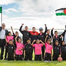 Boys in football jerseys pose with their fists in the air in front of the flags of Ireland and Palestine