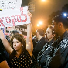 A pair of Israeli police officers, one a woman and the other a man, watch as a protesting woman holds a Hebrew-language sign over her head