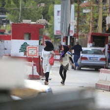 A woman and girl walk in front of car at checkpoint painted with colors and emblem of Lebanese flag
