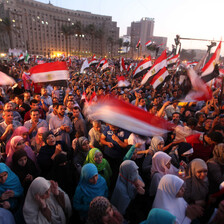 Crowd of hundreds of men and women wave Egyptian flags in public square