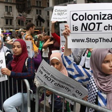 Young women hold up signs reading: Colonization is NOT charity www.stoptheJNF.org