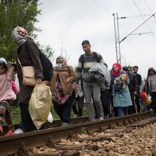 Men, women and children walk along railroad tracks while carrying their possessions