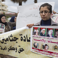 A woman holds a banner and a poster showing photos of slain men whose bodies are being held by Israel