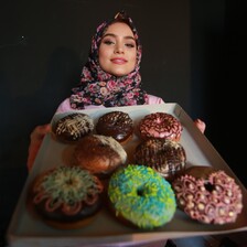 Young woman holds up a tray of doughnuts with varying toppings