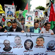Group of men hold banner showing images of jailed Palestinians in front of crowd of people holding up Palestinian flags and posters of prisoners
