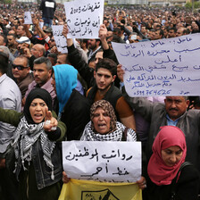 Men and women hold Arabic-language signs protesting salary cuts during large demonstration