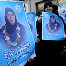 Close-up of poster being held by women showing Lina al-Jarbouni wearing a garland of flowers around her neck 
