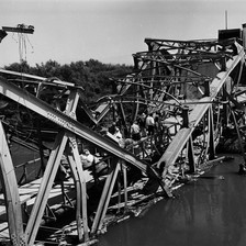 Black and white photo shows people walking across badly damaged bridge