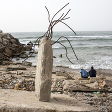 Photo shows the backs of two youths sitting on a beach strewn with litter and rubble