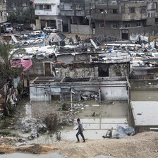 Wide view of boy walking in front of flooded neighborhood of shanty dwellings