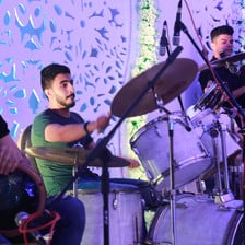 Close-up on young man playing on a drum kit with a tabla player and two singers standing on either side of him