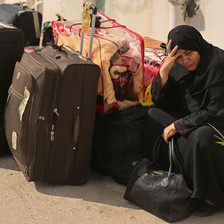 Middle-aged woman sitting on curb amid suitcases holds her head in her hand
