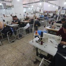 Photo shows men working at sewing machines in garment factory