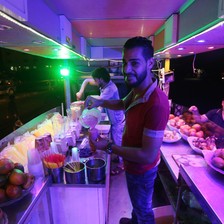 Smiling young man pours smoothie mix into a plastic cup at an outdoor juice stand