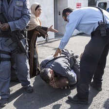 Elderly woman gestures her arm towards police officer as he stands over another officer who has pinned man to the ground