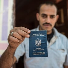 Man holds up passport-style document that says Arab Republic of Egypt Travel Document for Palestinian Refugees