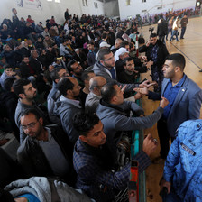 Dozens of people sit in the bleachers of a gymnasium used as a waiting area