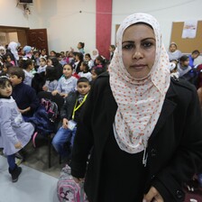 A young woman looking at the camera stands in front of a crowded hall of schoolchildren