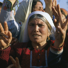 Elderly woman wearing traditional embroidered dress gives victory hand sign among crowd of women