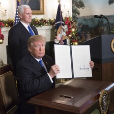 Trump sits at desk holding up newly signed executive order as Vice President Pence stands behind him