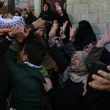 Photo shows crying women waving their hands at shrouded body of young man being carried on stretcher