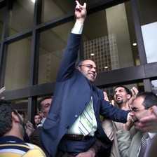 Man in middle of crowd smiles while making victory hand gesture outside court building
