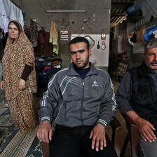 Father and son sit in chairs as mother stands behind them next to clothing line