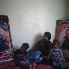 Woman and three small children sit on floor next to two large posters of smiling young man