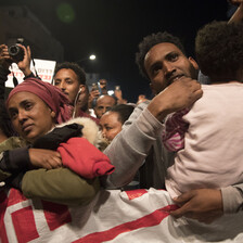 Man holding toddler and woman stand with their arms folded over protest banner