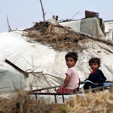 Photo shows small children sitting in front of tent shelter