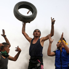 Young man holds tire above his head as other protesters clap and celebrate around him