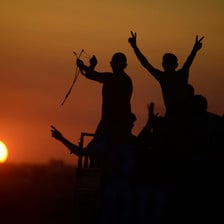 Silhouettes of protesters making V for victory signs and holding slingshots are seen against a setting sun