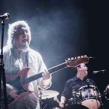 Concert photo of Richard Dawson playing guitar on stage with drummer in background