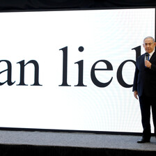 Netanyahu stands on stage with Iran lied in giant letters projected on a screen behind him