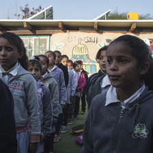 Schoolchildren stand in rows in front of single-story school