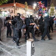 Security forces carrying rifles and wearing all black and face masks walk through city center