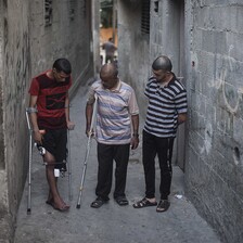 Three men stand in an alley, two of them using crutches.