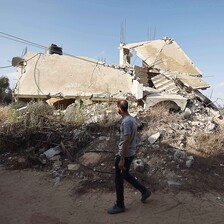 A man holding a cigarette walks past a collapsed building