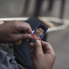 Close-up photo of two hands holding a passport-size image of a smiling baby