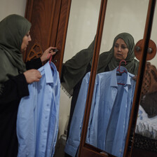 Woman holds shirt, while looking into mirror