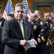 Peter King, a member of Congress for New York, stands beside US flags and soldiers in uniform.