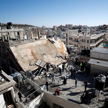 Landscape view of people standing on rooftops adjacent to destroyed building