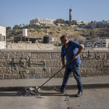 A man pushes trash with a broom along a street